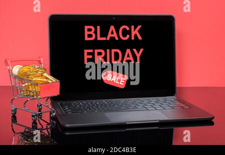Concetto per il Black Friday online e vendite invernali con shopping cart pieno di monete d'oro di fronte ad un moderno computer portatile che annuncia la vendita Foto Stock