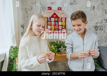 I bambini che leggono i compiti dal calendario dell'avvento fatto a mano di Natale in una forma di casa per conto alla rovescia i giorni fino a Natale sul muro nella stanza. Selez Foto Stock