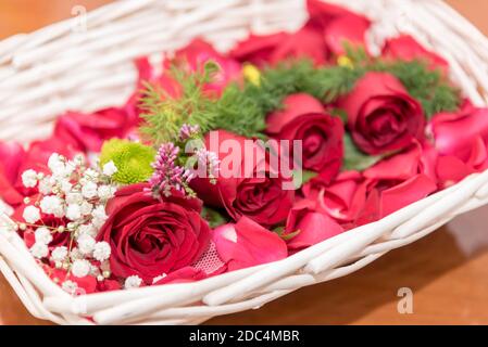 grazioso cestino di rose rosse adornato con fiori verdi e. petali di rosa Foto Stock