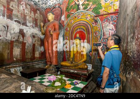 Un uomo filma all'interno della colorata Grotta uno (Devaraja Viharaya) ai Templi della Grotta di Dambulla nello Sri Lanka. All'interno della grotta si trova una statua del Buddha seduto. Foto Stock