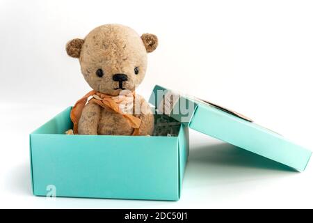 Un piccolo orsacchiotto vintage fatto a mano si trova in una scatola regalo su uno sfondo bianco. Regalo e sorpresa per una vacanza importante. Primo piano. Spazio di copia. Foto Stock