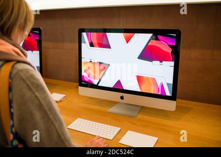 Parigi, Francia - 16 novembre 2019: Vista laterale della donna che guarda i più recenti computer Apple iMac 27 21 pollici personal computer con pubblicità sullo schermo 5k per il nuovo orologio Apple con più band Foto Stock