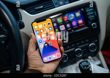 Parigi, Francia - 11 novembre 2020: Mano maschile che tiene il nuovo iPhone 12 pro con le icone del sistema di infotainment computer auto che esegue Apple computer CarPlay da iOS iphone dispositivo Foto Stock