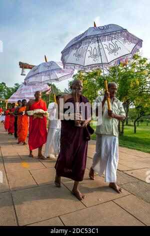 Monaci buddisti protetti da ombrelli dal sole del pomeriggio portano offerte verso la Ruwanwelisiya Dagoba ad Anuradhapura in Sri Lanka. Foto Stock