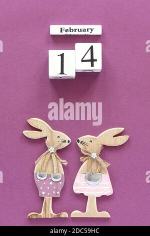 Composizione romantica cubi di legno calendario 14 febbraio e coppia di amanti del legno figurine conigli su sfondo viola. Carta di San Valentino Concept. Da a. Foto Stock