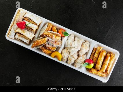 Vari tipi di pasticceria e torte con marzapane in piatti bianchi su cemento nero. Foto Stock