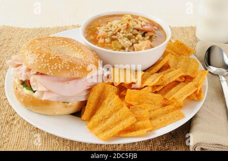 Un sandwich di prosciutto su un bagel con gumbo di salsiccia di pollo e patatine naturali Foto Stock