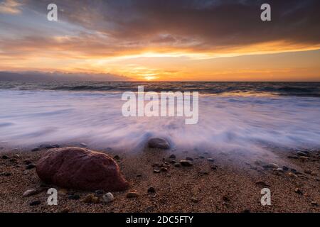 Un Rush of Wave Water arriva alla Shore AS Il sole si imposta sull'orizzonte dell'oceano Foto Stock