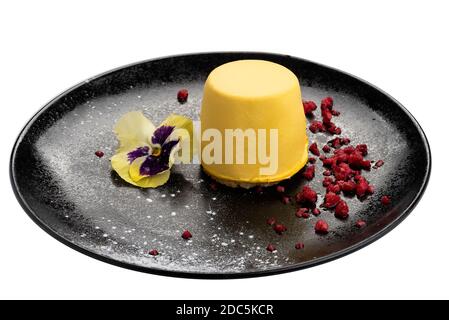 Cheesecake di mango su piatto nero guarnito con polvere dolce di fragola rossa e fiore. Isolato su sfondo bianco Foto Stock
