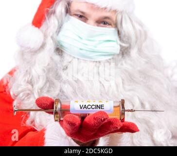 Babbo Natale con maschera facciale offre un'iniezione di vaccino. Foto Stock