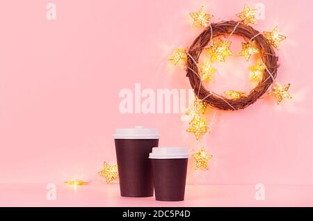 Mock up caffè di Natale - due tazze di carta nera, stelle d'oro e luci in corona su sfondo rosa, modello per la pubblicità, il design, caffè, ristorante Foto Stock