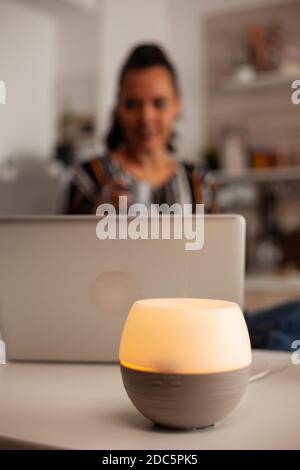 Donna che usa il computer portatile godendo di aromaterapia dal diffusore di olio Aroma essenza di salute, benessere casa fragranza spa tranquilla terapeuta, vapore terapeutico, trattamento di salute mentale Foto Stock