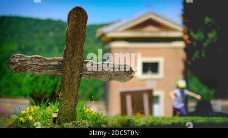 vecchia croce di legno nel cimitero con piccola chiesa sul sole giorno con la bambina che corre in background Foto Stock