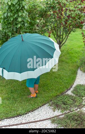 Bambino sotto un grande ombrello verde in giardino Foto Stock