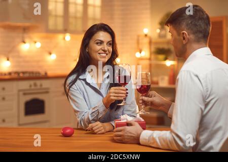 Giovane coppia affettuosa felice che si guarda l'un l'altro e si aggraffa bicchieri con vino Foto Stock