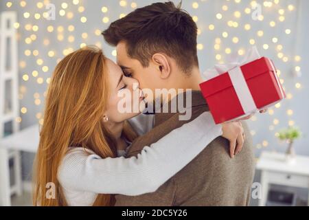 Vista laterale di una bella giovane donna che bacia il marito sulla guancia in gratitudine per un regalo. Foto Stock