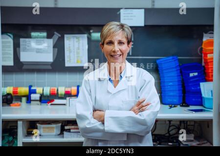 Esame del camice da laboratorio bianco con braccio incrociato da parte di una farmacista senior recupero del farmaco in laboratorio Foto Stock