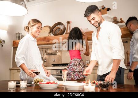 Bei millennials amici gruppo di legame a casa preparare spuntini per Aperitivo - due coppie eterosessuali che si divertono insieme nel cucina cucina Foto Stock