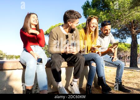 Due giovani e belle coppie eterosessuali che si ridono l'un l'altro utilizzando lo smartphone A chattare online - felice gruppo millenario di persone che hanno divertimento all'aperto Foto Stock