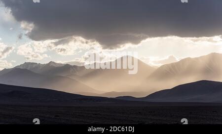 Montagne con raggi solari e nebbia vicino Karakul con vista su alte montagne nere, deserto e valle in Tagikistan. Foto Stock