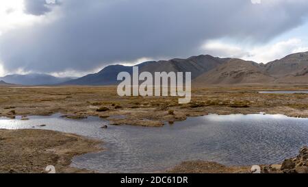 Montagne e paludi nei pressi di Karakul con vista su alte montagne nere, deserto e valle in Tagikistan. Foto Stock