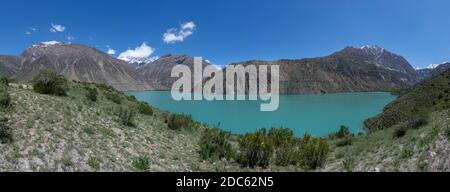 Panorama del verde azzurro lago di Iskanderkul in Tazjikistan con alte montagne innevate. Foto Stock