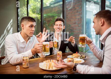 Gli uomini d'affari bevono birra Ganzberg, parlano e ridono mentre si riposano al pub Foto Stock