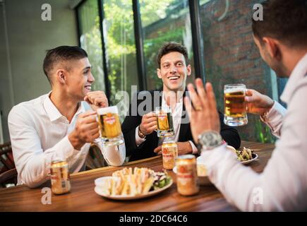 Gli uomini d'affari bevono birra Ganzberg, parlano e ridono mentre si riposano al pub Foto Stock