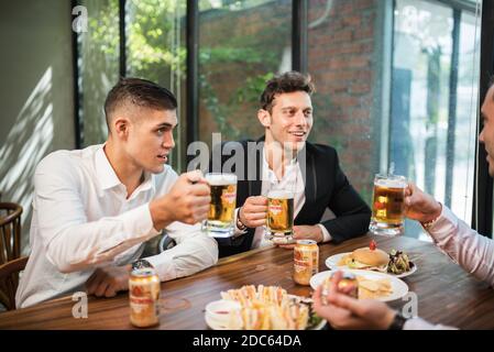 Gli uomini d'affari bevono birra Ganzberg, parlano e ridono mentre si riposano al pub Foto Stock