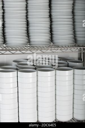 Un colpo delle pile di molte piastre bianche su un scaffale a griglia in una cucina commerciale Foto Stock