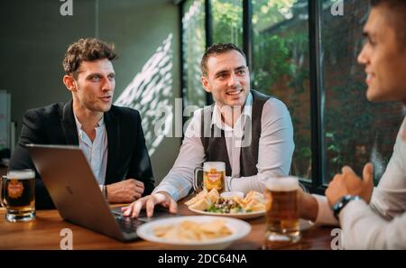 Gli uomini d'affari bevono birra Ganzberg, parlano e ridono mentre si riposano al pub Foto Stock