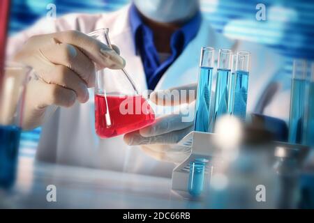 Dettaglio di uno scienziato che manipola con cura un liquido rosso in un pallone su un tavolo da laboratorio. Composizione orizzontale. Vista frontale. Foto Stock