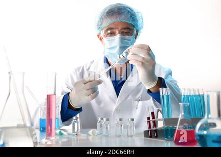 Personale medico dotato di protezione personale che carica le dosi da una fiala su un tavolo da laboratorio con campioni e vetreria. Vista frontale. Orizzontale Foto Stock