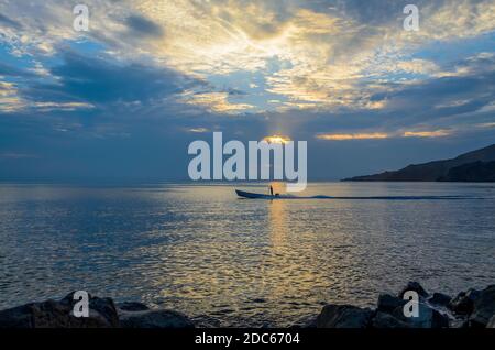 Silhouette di un pescatore solista in una barca da pesca che inizia per il lavoro durante la prima luce del mattino. Foto Stock