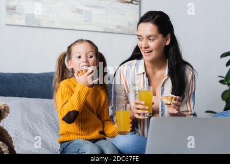 figlia che mangia deliziosi muffin mentre guarda film sul computer con madre Foto Stock