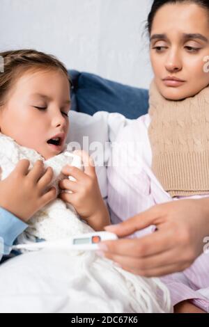 turbare la madre che tiene il termometro mentre la figlia malata usando lo spruzzo della gola Foto Stock