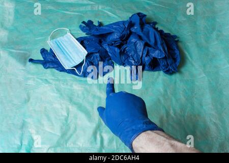 Un dito guanto blu punta a un mucchio di attrezzature per la cura personale indossate in ambito sanitario collocato su un tavolo coperto di tessuto chirurgico verde. Foto Stock