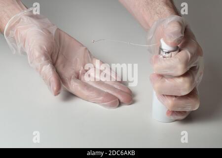 La mano sinistra utilizza un dispenser di gel idroalcolico per spruzzare un flusso di gel disinfettante sulla mano destra del guanto. Foto Stock