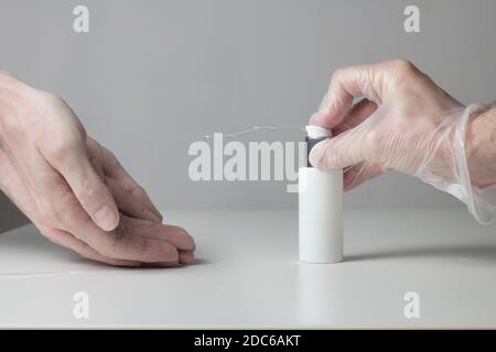 Un getto di gel disinfettante idroalcolico fuoriesce dalla bottiglia premuta da una mano guanto mentre le mani sporche attendono di ricevere il liquido. Foto Stock