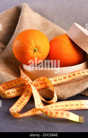 Frutta messa in confezione su sacco. Frutta arancione di colore succoso su fondo di tessuto beige. Arance in ecbox rotondo in legno legato con arco di nastro di misurazione giallo. Concetto sano di cibo organico. Foto Stock