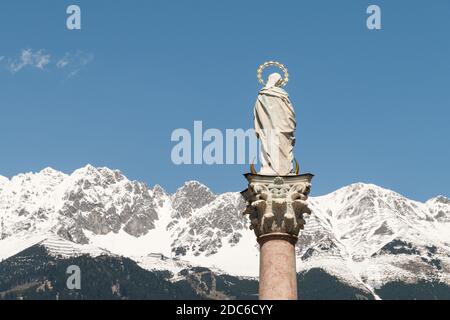 Primo piano da dietro la Vergine Maria in cima alla colonna di Sant'Anna a Innsbruck, Austria. Le montagne innevate delle Alpi sono sullo sfondo. Foto Stock