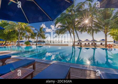 Lussuoso resort sulla spiaggia con piscina e sedie a sdraio o lettini sotto ombrelloni con palme e cielo blu. Viaggio estivo e vista vacanza Foto Stock