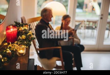Candele brucianti e rami di abete su mantelpiece con la videochiamata di coppia senior in background. Casa Sandinava decorata per le vacanze di Natale. Foto Stock