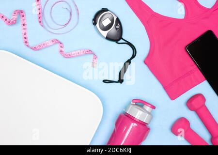 Bilancia per il peso del corpo, reggiseno sportivo, cronometro digitale, manubri, bottiglia d'acqua, nastro di misurazione, layout smartphone. Donne perdita di peso sport di formazione, fitnes Foto Stock