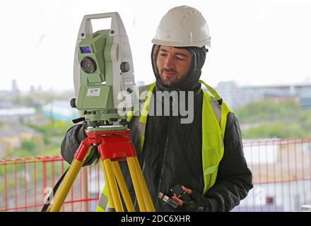 Un topografo di costruzione maschile regola una teodolite elettronica su un Grande sviluppo londinese Foto Stock