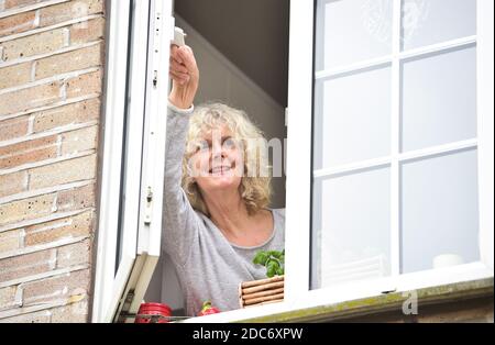 Donna a casa che apre la finestra della cucina per lasciare in fresco Air come consigliato per aiutare a combattere il virus COVID-19 del coronavirus Foto Stock