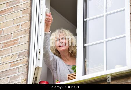 Donna a casa che apre la finestra della cucina per lasciare in fresco Air come consigliato per aiutare a combattere il virus COVID-19 del coronavirus Foto Stock