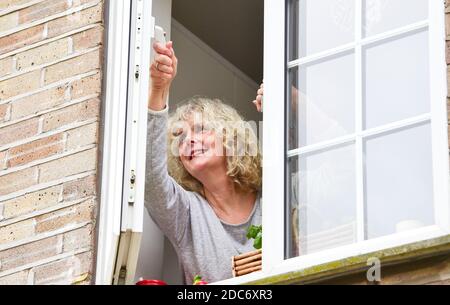 Donna a casa che apre la finestra della cucina per lasciare in fresco Air come consigliato per aiutare a combattere il virus COVID-19 del coronavirus Foto Stock