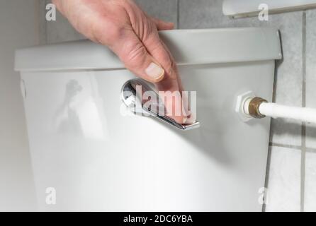 Primo piano POV colpo di una mano di un uomo che spinge il manico per lavare una cassetta di ceramica bianca della toilette del bagno. Foto Stock