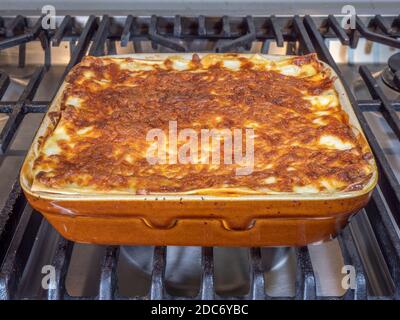 Primo piano POV di pasta fatta in casa, cucinata di fresco, bollente lasagne, in una piastra di cottura in ceramica, su un piano cottura. Foto Stock